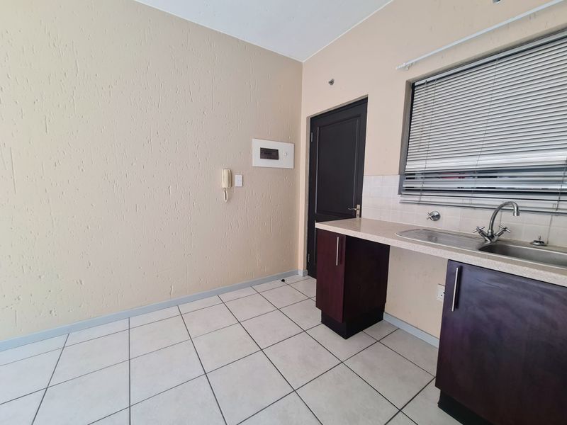 A functional kitchen area featuring tiled flooring, base cabinetry with a laminate countertop, a stainless steel sink, and an integrated intercom system.