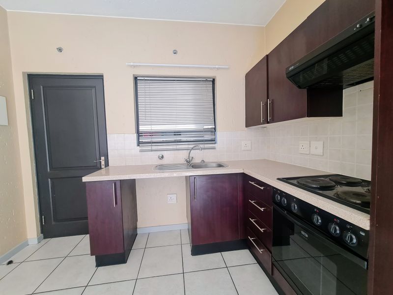 A functional kitchen featuring dark wood cabinetry, laminate countertops, a built-in oven with hob, and tiled flooring, offering a clean and practical workspace.
