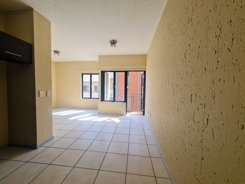 An empty open-plan living area featuring tiled flooring, textured walls, and a sliding glass door leading to a balcony.