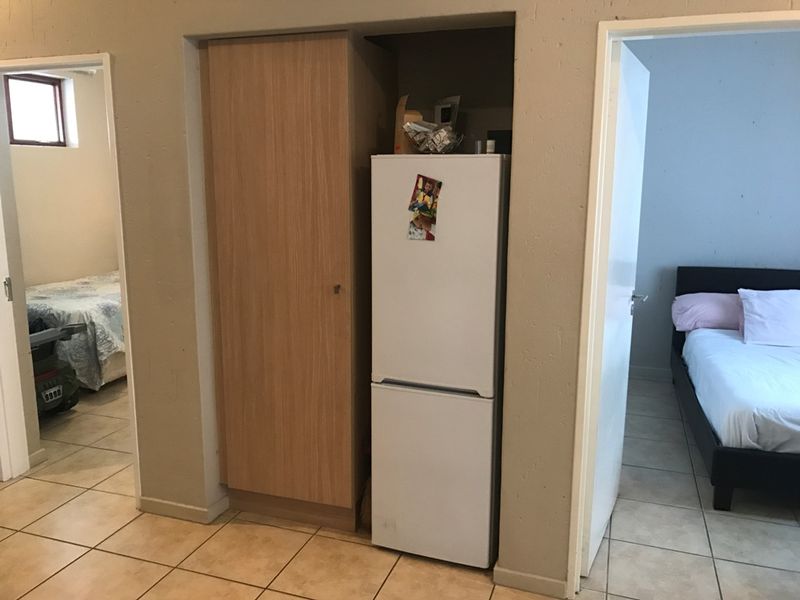 A functional hallway area featuring tiled flooring and a built-in cupboard, providing access to adjacent bedrooms.