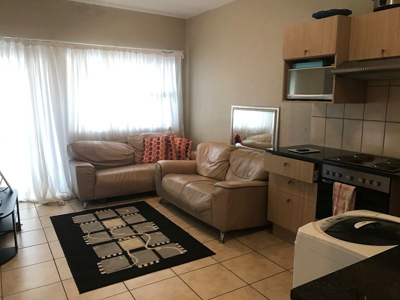 Open-plan living area featuring tiled flooring and a compact kitchen with built-in cabinetry, electric stove, and extractor fan.