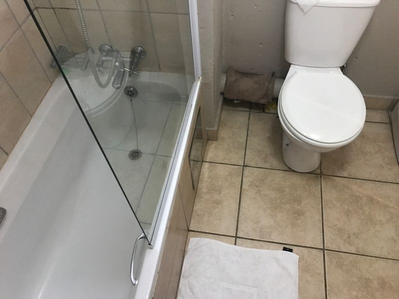 A functional bathroom featuring a bathtub with a glass shower screen, a standard toilet, and tiled flooring and wall finishes.