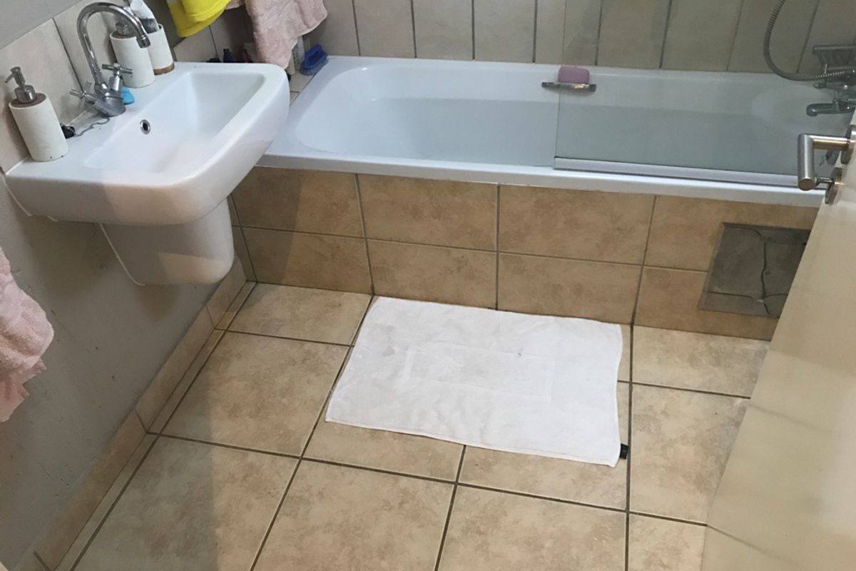 A functional bathroom featuring a pedestal basin, a built-in bathtub with a glass shower screen, and neutral ceramic tiling throughout.