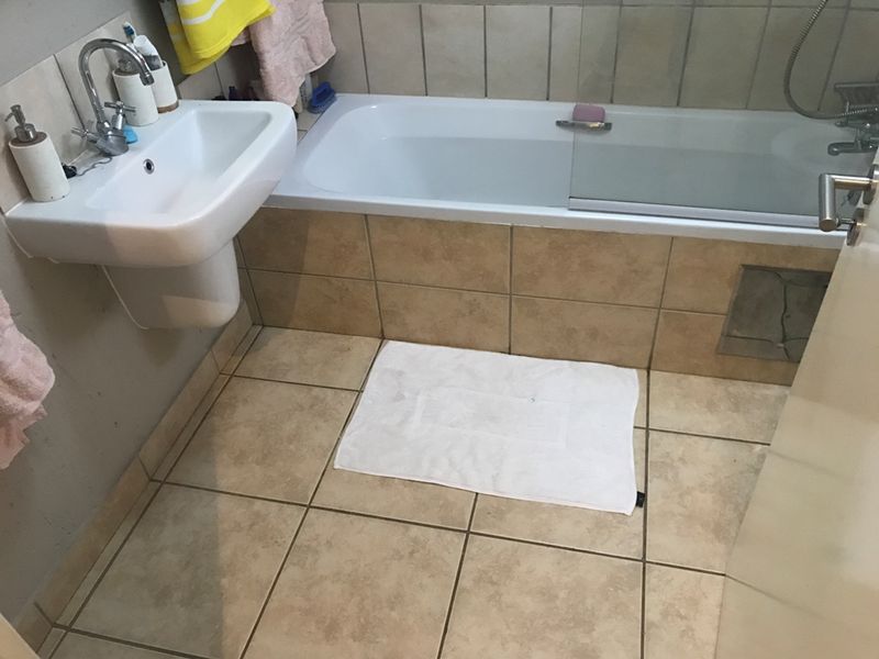 A functional bathroom featuring a pedestal basin, a built-in bathtub with a glass shower screen, and neutral ceramic tiling throughout.