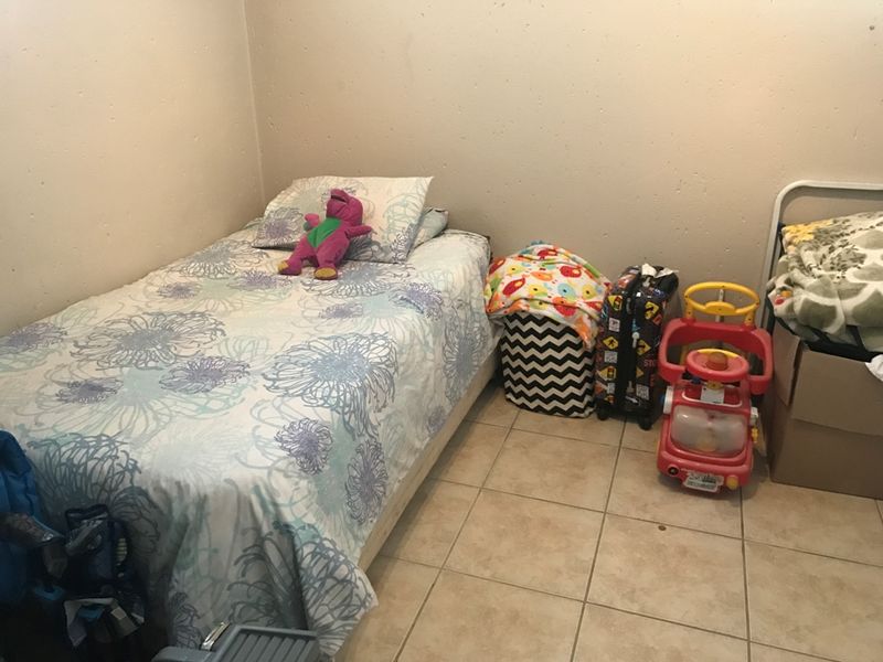 A compact bedroom featuring tiled flooring and plain walls, currently utilized as a child's sleeping area.