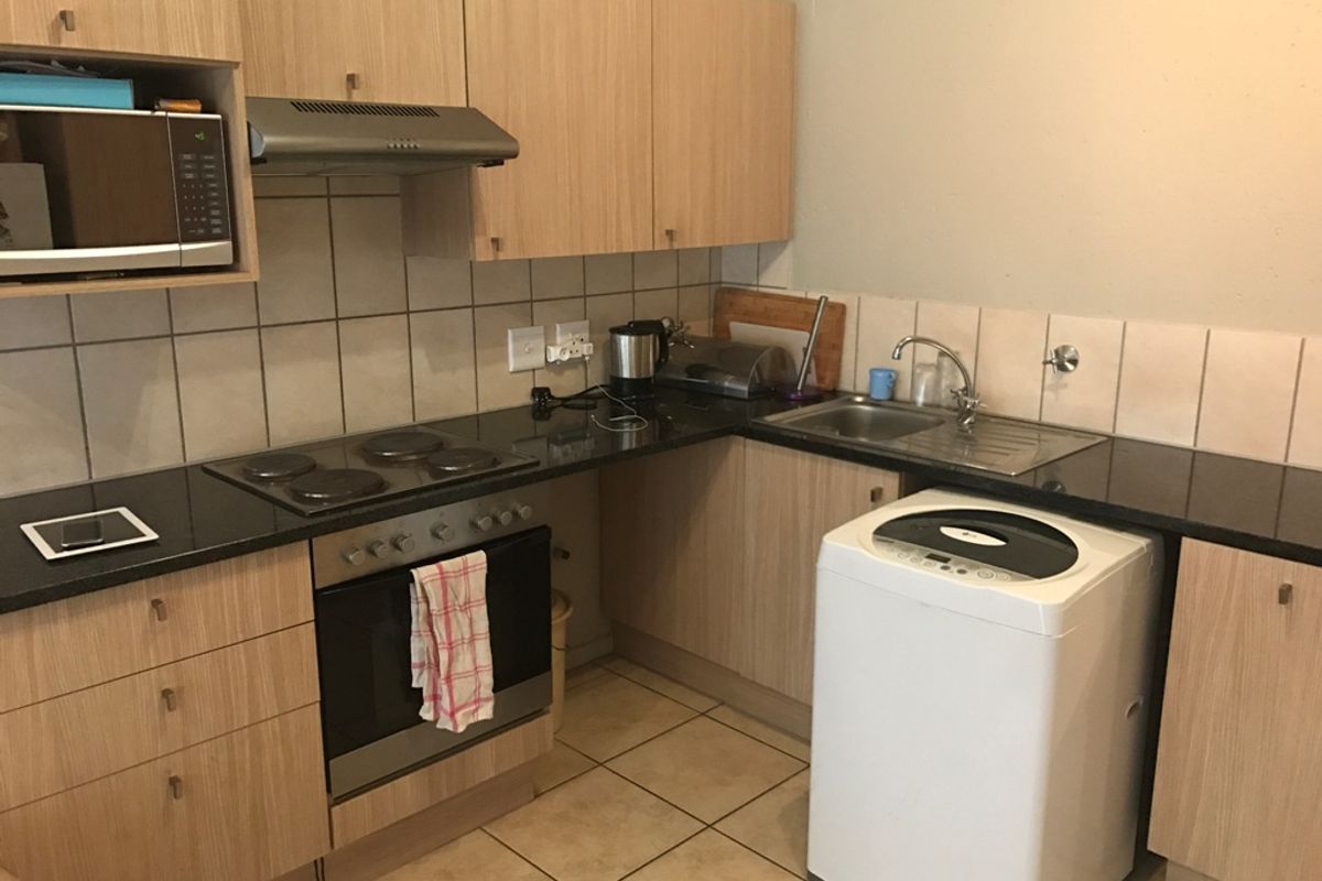 A functional kitchen featuring light wood-finish cabinetry, dark countertops, a built-in oven and hob, and tiled flooring with a dedicated space for laundry appliances.