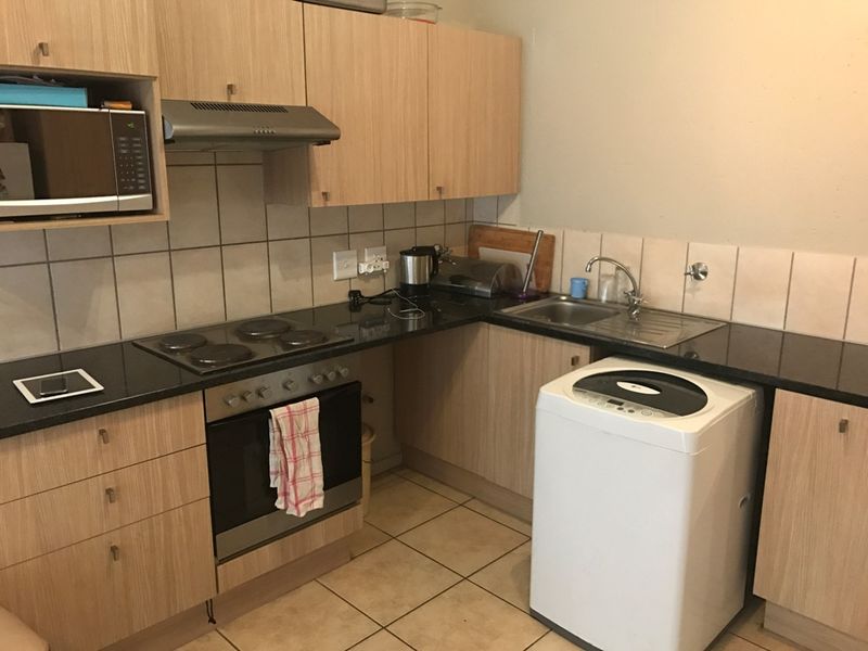 A functional kitchen featuring light wood-finish cabinetry, dark countertops, a built-in oven and hob, and tiled flooring with a dedicated space for laundry appliances.