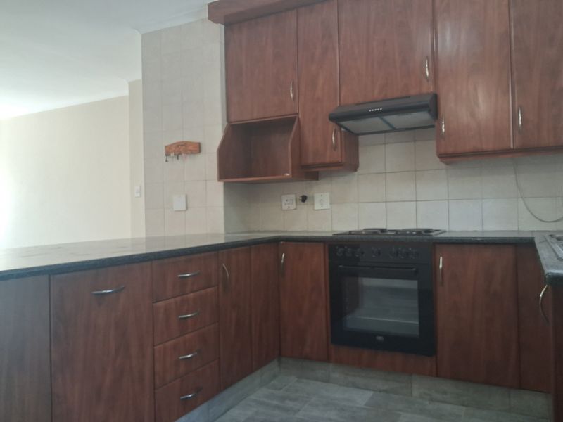 A functional kitchen featuring wood-look laminate cabinetry, granite countertops, and built-in cooking appliances, including an oven, hob, and extractor fan.