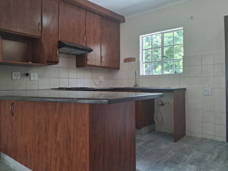 A functional kitchen featuring dark wood cabinetry, granite countertops, a tiled backsplash, and a built-in extractor fan, offering a clean and practical workspace.