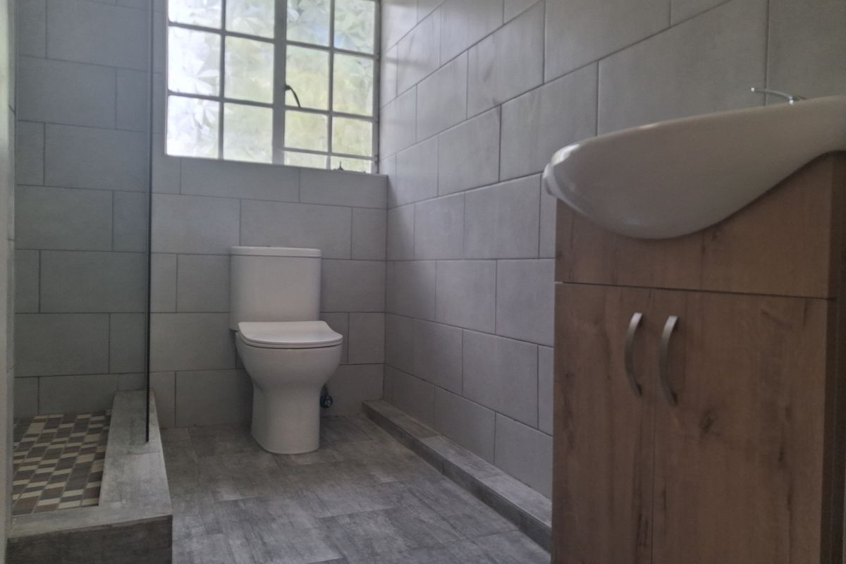 A modern bathroom featuring a walk-in shower, a vanity cabinet with a basin, and a toilet, finished with neutral wall and floor tiles.