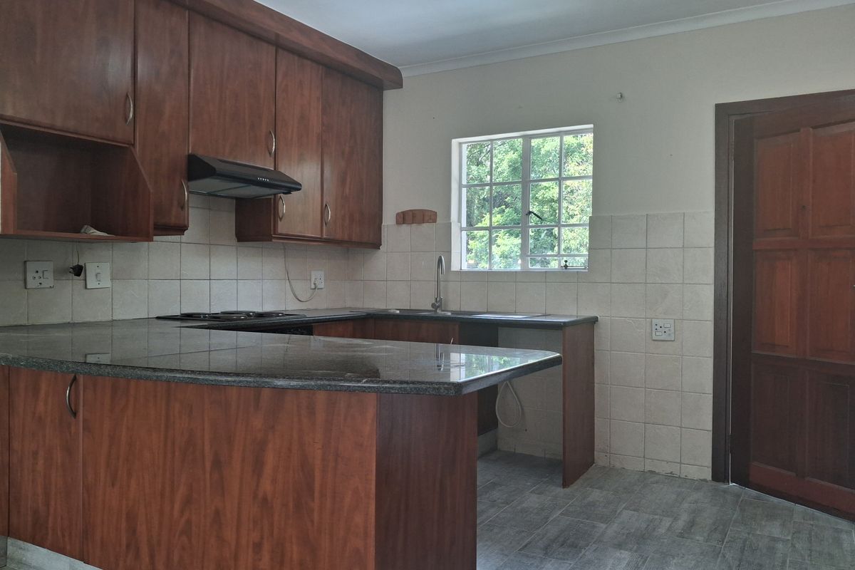 A functional kitchen featuring wooden cabinetry, granite countertops, a built-in hob with extractor fan, and tiled flooring.