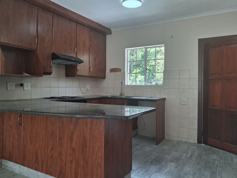 A functional kitchen featuring wooden cabinetry, granite countertops, a built-in hob with extractor fan, and tiled flooring.