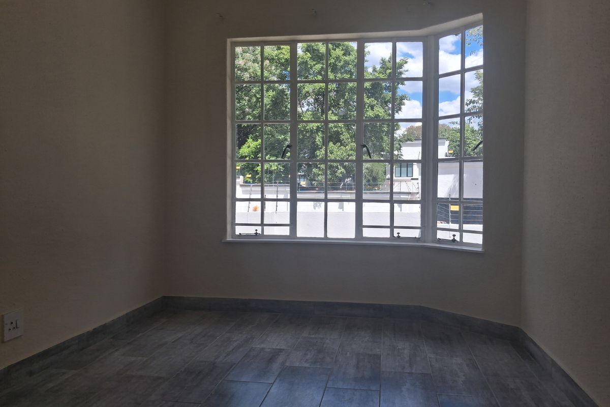 A bright, empty bedroom featuring modern grey tiled flooring and a large bay window that allows for ample natural light.