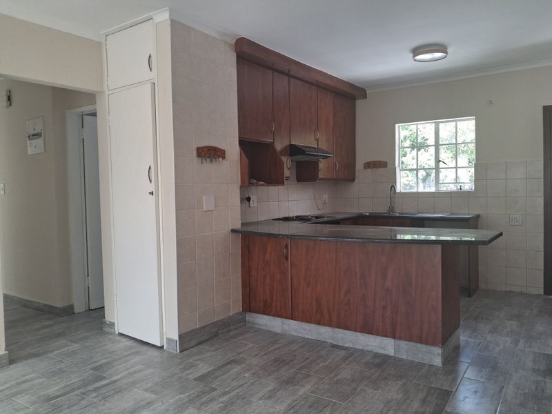 A functional kitchen featuring dark wood cabinetry, laminate countertops, a built-in hob with extractor fan, and tiled flooring in an open-plan layout.