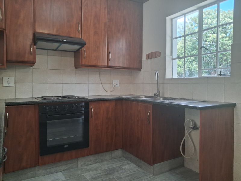 A functional kitchen featuring wood-look cabinetry, a built-in oven with hob, extractor fan, and a stainless steel sink with tiled backsplash.