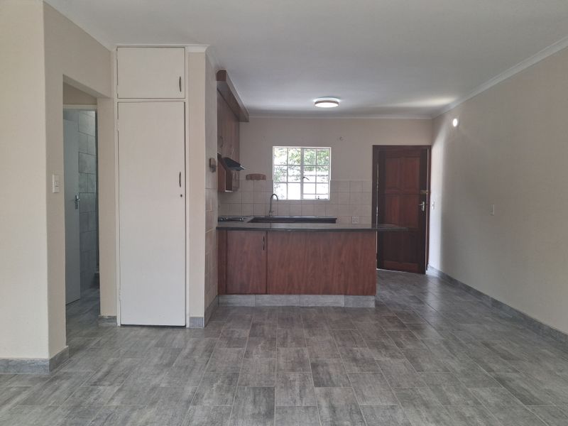 An open-plan living and kitchen area featuring modern grey tiled flooring, built-in wooden cabinetry, and a functional kitchen island with a sink.