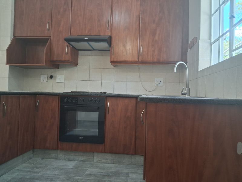 A functional kitchen featuring wooden cabinetry, built-in oven with hob, extractor fan, and tiled finishes, offering a clean and practical workspace.