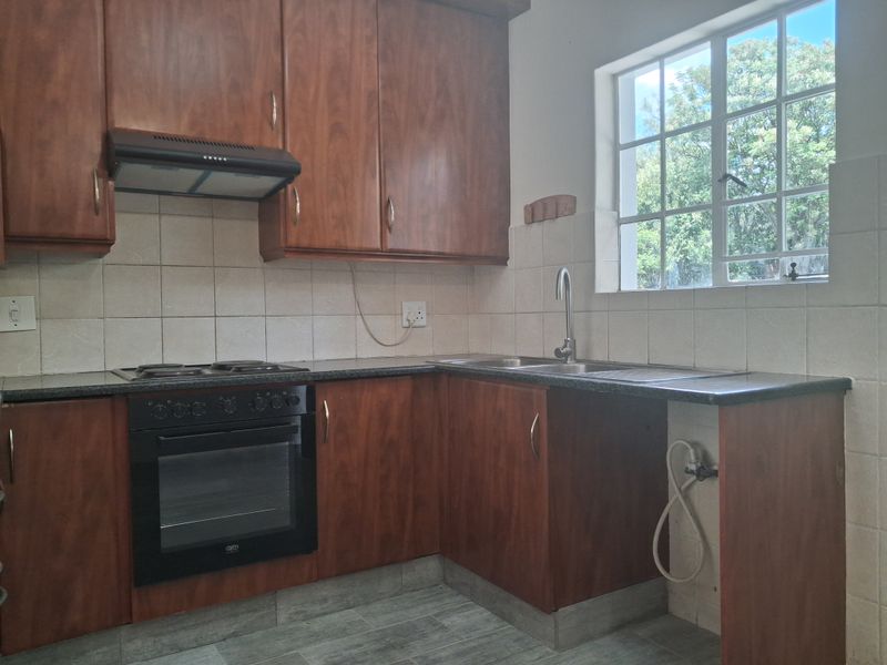 A functional kitchen featuring wood-finish cabinetry, built-in oven and hob, tiled backsplash, and a window providing natural light.