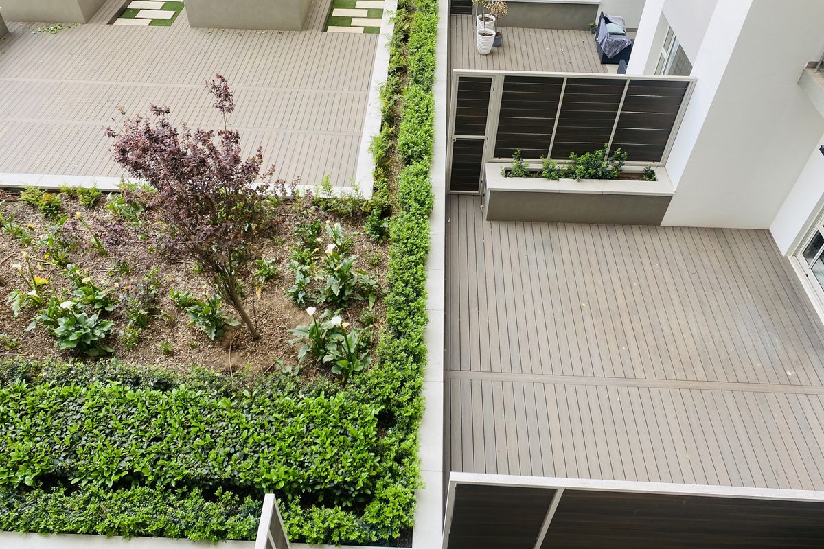 An elevated view of a modern apartment complex featuring well-maintained composite decking, landscaped garden beds, and integrated privacy screens.