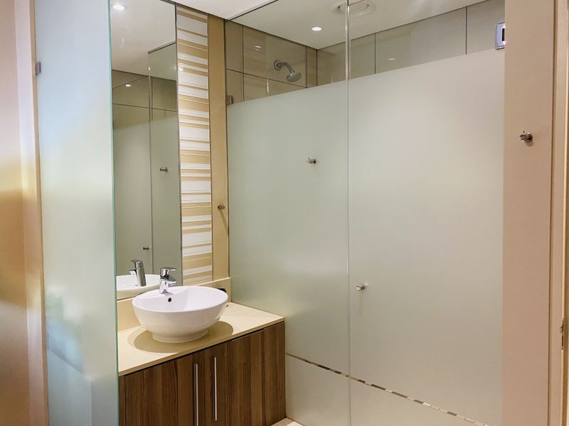 Modern bathroom featuring a vessel sink with vanity cabinet and a spacious walk-in shower with a frosted glass screen.