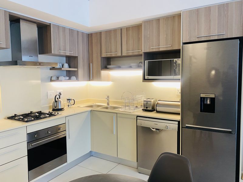 Modern kitchen featuring wood-tone and cream cabinetry, stainless steel appliances including a gas hob, oven, extractor fan, and integrated dishwasher with under-cabinet lighting.