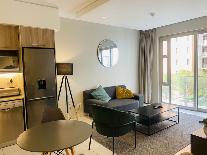 Modern open-plan living area featuring a compact kitchen with built-in cabinetry and seamless access to a private balcony through large sliding glass doors.