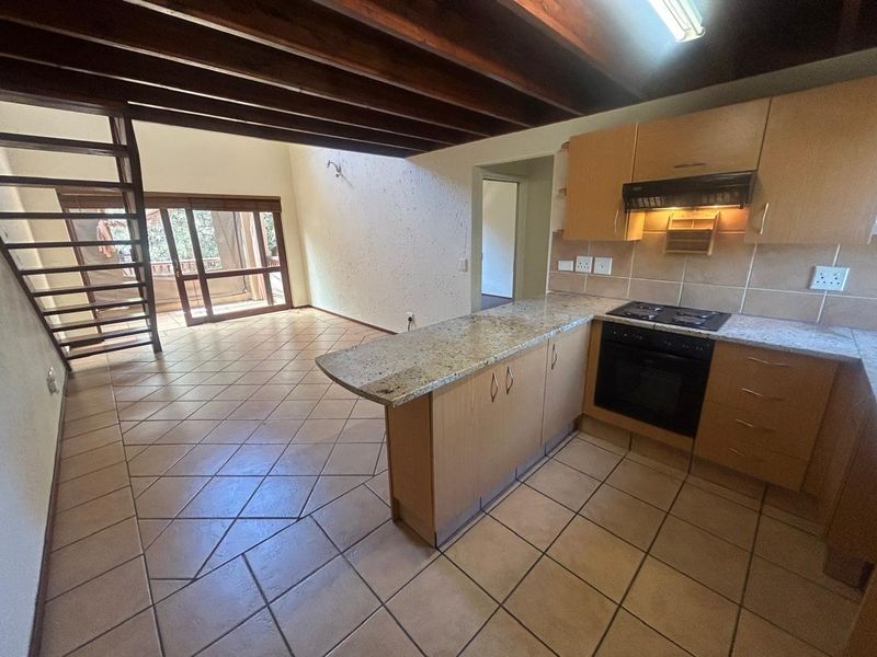 Open-plan kitchen and living area featuring tiled flooring, exposed timber beams, built-in cabinetry with granite countertops, and a staircase leading to an upper level.