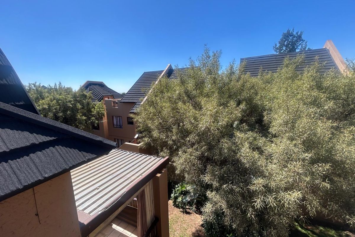 An elevated view of the apartment complex exterior, featuring tiled roofing, a balcony, and surrounding mature trees.