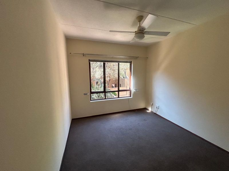 A vacant bedroom featuring neutral walls, carpeted flooring, and a ceiling fan, offering a blank canvas for personalization.