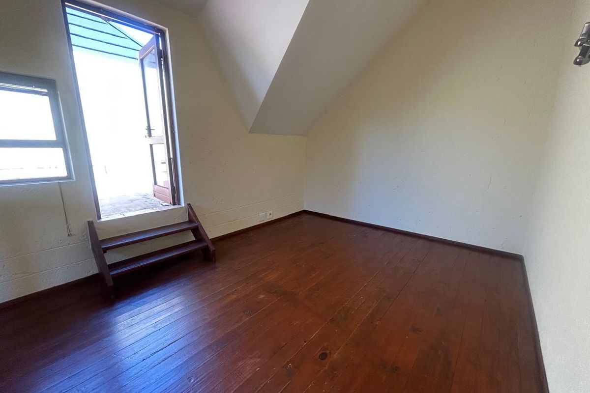 An empty bedroom featuring timber flooring, a sloped ceiling, and direct access to an outdoor balcony area.