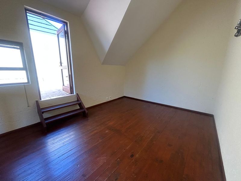 An empty bedroom featuring timber flooring, a sloped ceiling, and direct access to an outdoor balcony area.