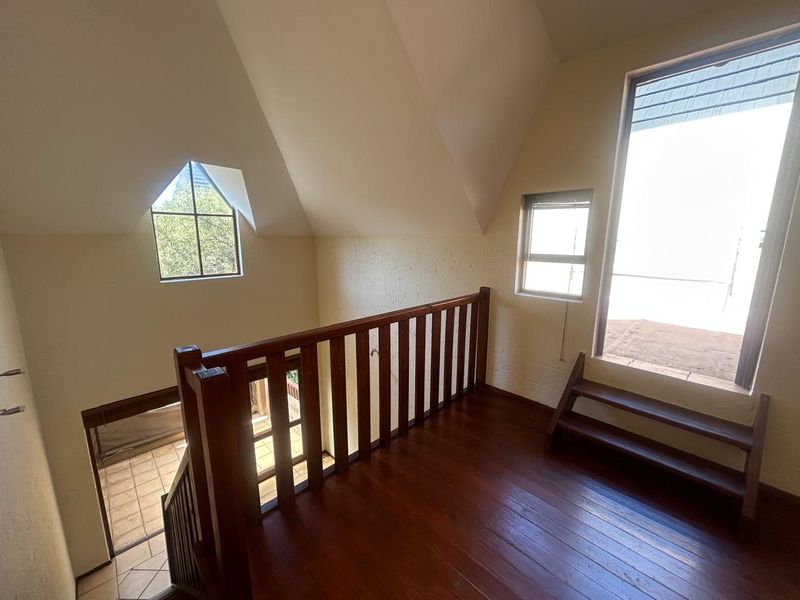 A bright, open landing area featuring timber flooring, a wooden balustrade, and a pitched ceiling with multiple windows providing natural light.