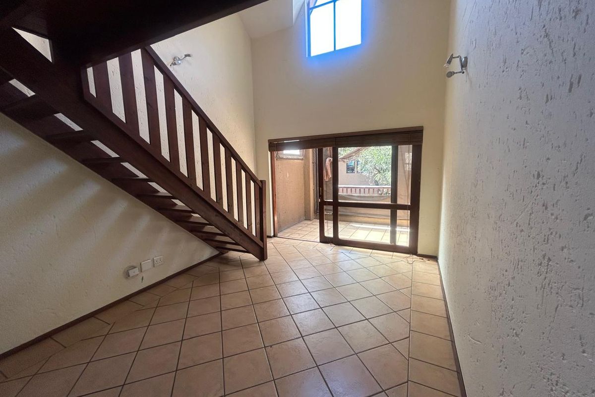 Spacious living area featuring high vaulted ceilings, a wooden staircase, tiled flooring, and large sliding glass doors leading to an outdoor space.