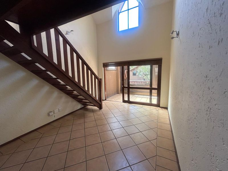 Spacious living area featuring high vaulted ceilings, a wooden staircase, tiled flooring, and large sliding glass doors leading to an outdoor space.