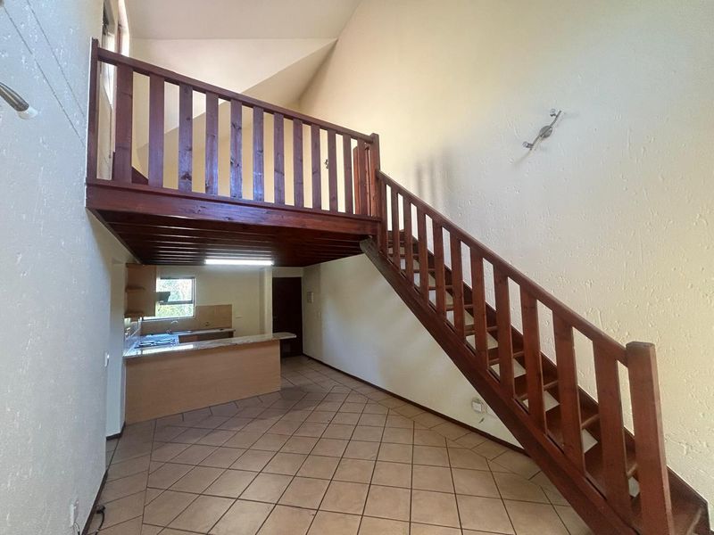 Open plan living area featuring a mezzanine level, wooden staircase, and a functional kitchen with granite countertops and tiled flooring.