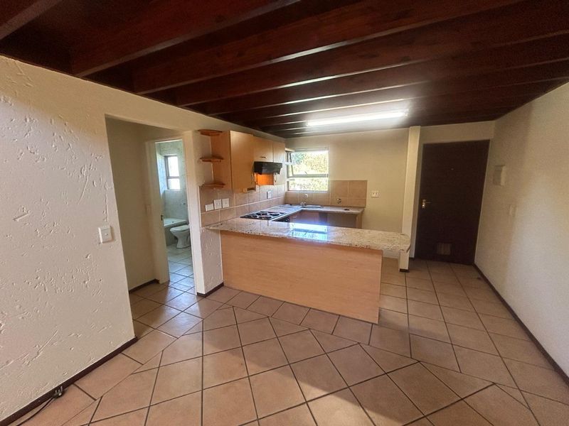 Open plan kitchen and living area featuring exposed timber ceiling beams, granite countertops, and tiled flooring, with an adjacent bathroom visible.