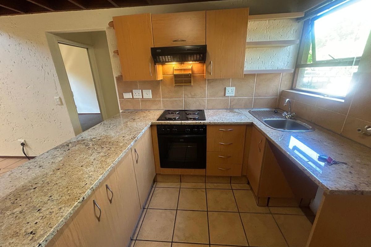 A functional kitchen featuring granite countertops, built-in oven, electric hob, and wooden cabinetry with tiled flooring and backsplash.