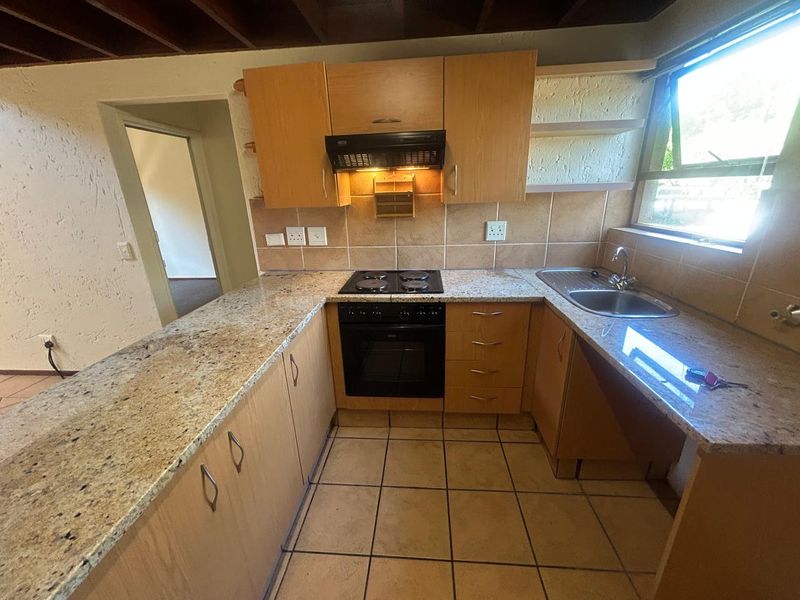 A functional kitchen featuring granite countertops, built-in oven, electric hob, and wooden cabinetry with tiled flooring and backsplash.