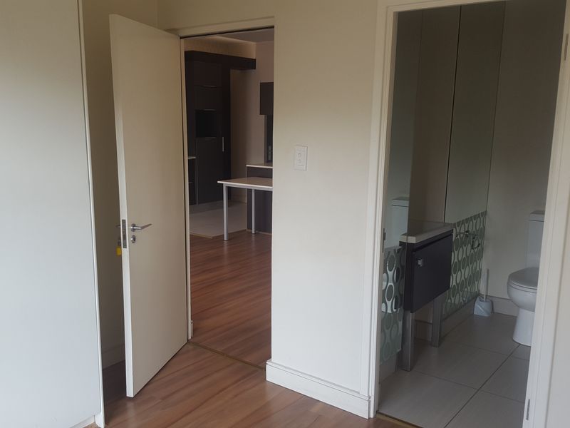 A view from a hallway looking into a bathroom and an adjacent living area, featuring laminate flooring and neutral wall finishes.