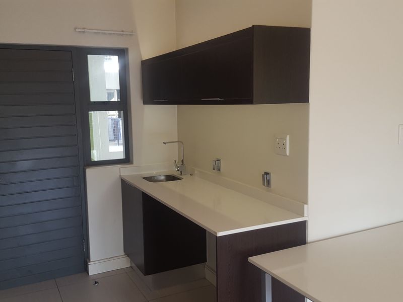 A clean, modern kitchen area featuring dark cabinetry, stone countertops, and a stainless steel sink, presented in an empty, well-maintained space.