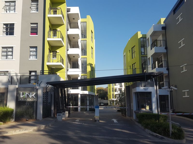 The main entrance and security gatehouse of the Link Rivonia apartment complex, featuring modern multi-story residential buildings with balconies and controlled access.
