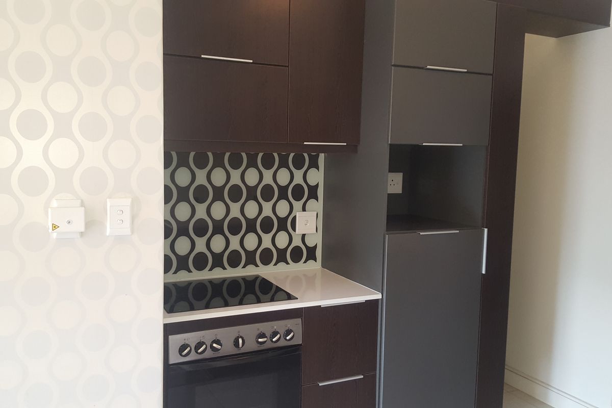 Modern kitchen featuring dark cabinetry, stone countertops, a built-in oven with electric hob, and a decorative patterned glass splashback.