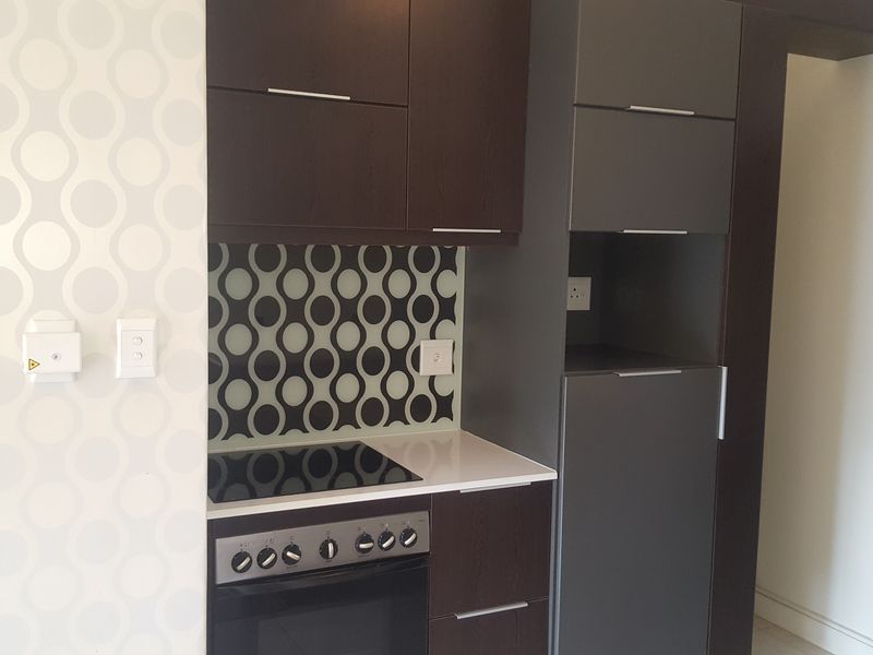 Modern kitchen featuring dark cabinetry, stone countertops, a built-in oven with electric hob, and a decorative patterned glass splashback.