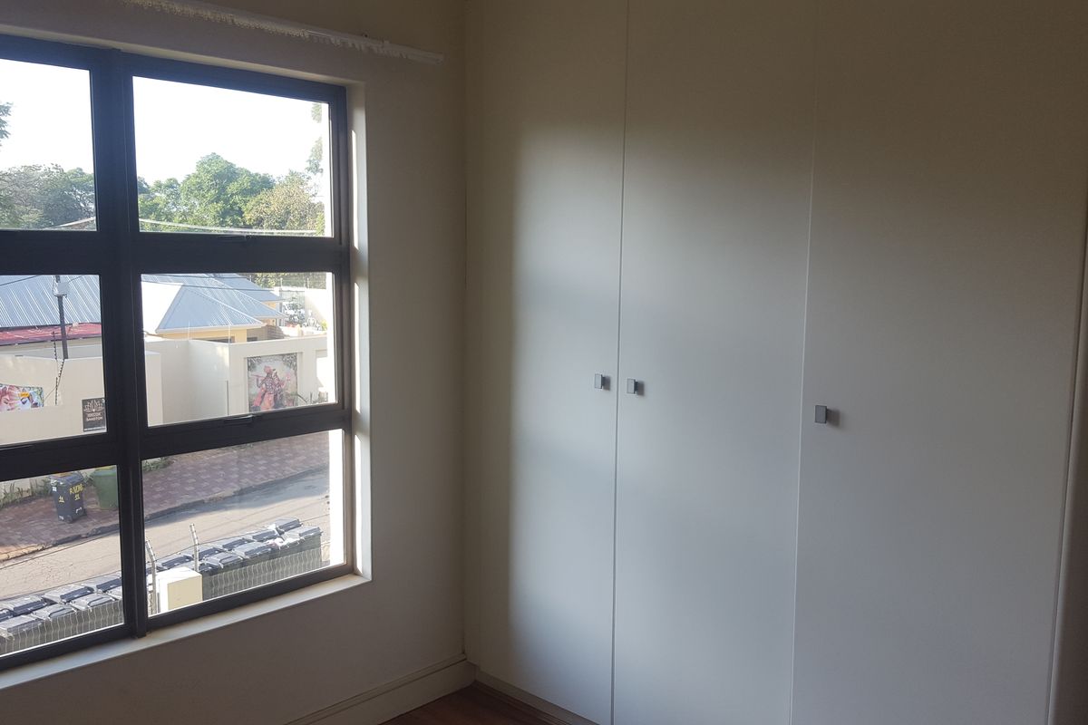 A bright, empty bedroom featuring modern built-in cupboards and a large window with views of the street.