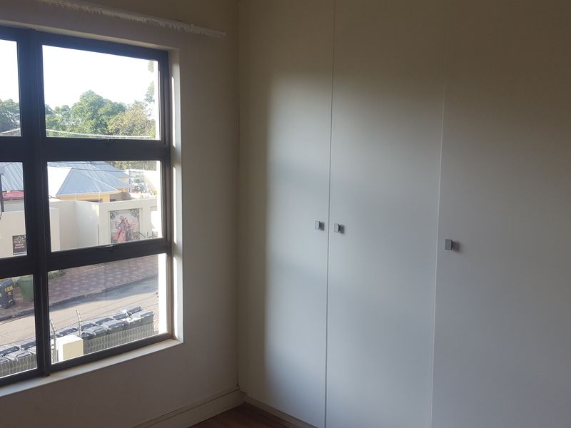 A bright, empty bedroom featuring modern built-in cupboards and a large window with views of the street.
