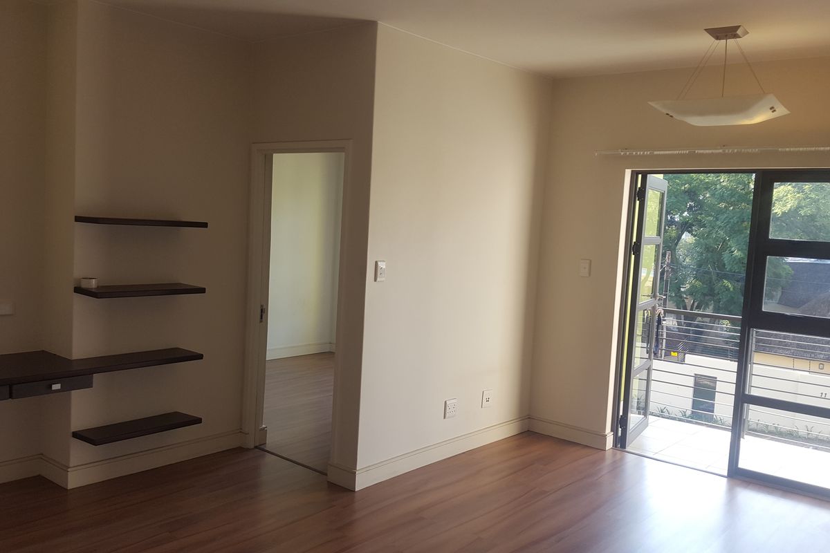 Bright living area featuring laminate flooring, built-in shelving, a desk nook, and a sliding glass door leading to an outdoor balcony.