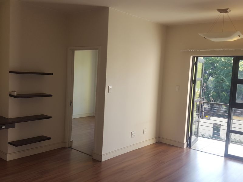 Bright living area featuring laminate flooring, built-in shelving, a desk nook, and a sliding glass door leading to an outdoor balcony.