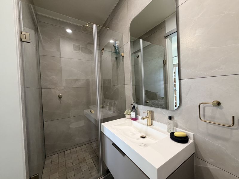 Modern bathroom featuring a walk-in shower with glass screen, wall-mounted vanity with basin, gold-tone fixtures, and contemporary large-format wall tiling.