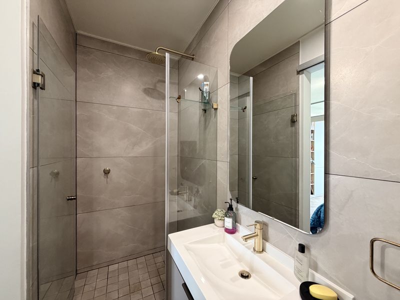 Modern bathroom featuring a walk-in shower with glass screen, rain shower head, brass tapware, and large wall mirror with neutral porcelain tiling.