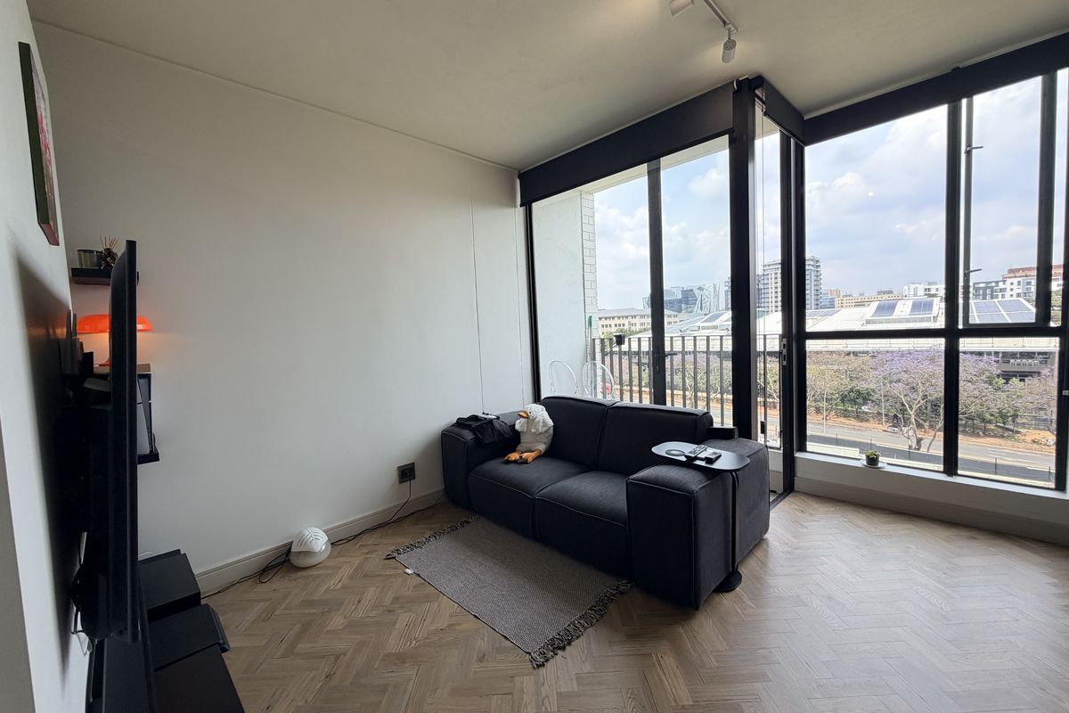 Modern living room featuring elegant herringbone timber flooring, floor-to-ceiling windows with black frames, and contemporary track lighting, offering an airy and bright atmosphere.